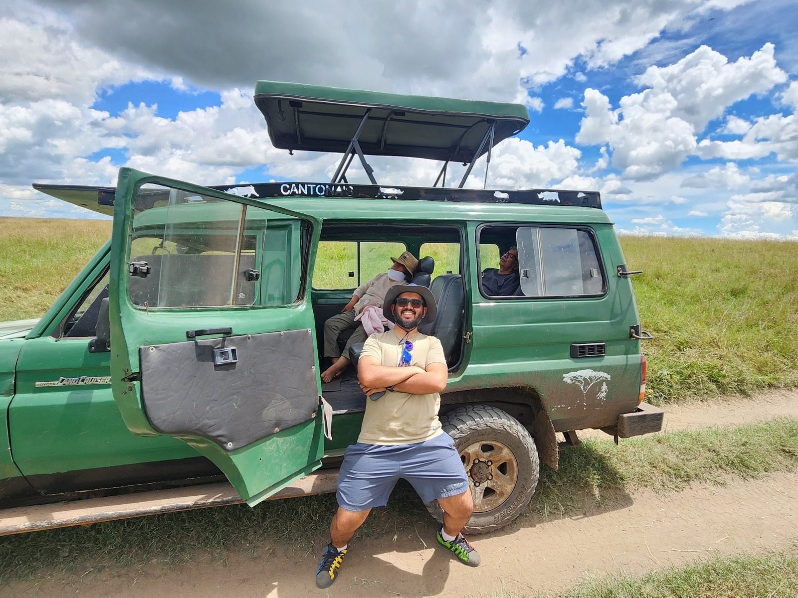 Nikhil sitting on the step of an open safari Land Cruiser on a game drive in the Maasai Mara.